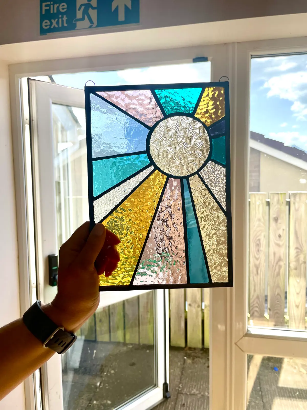 A finished stained glass panel of a stylised sun, held against the light